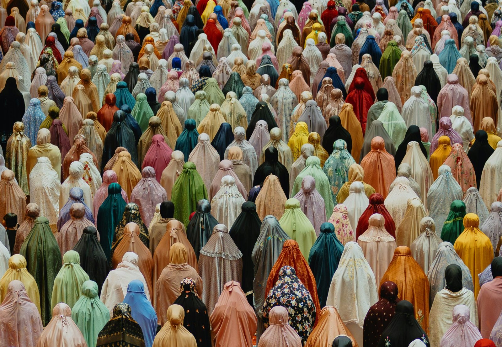Large gathering of Muslim women in colorful prayer garments seen from behind during communal prayer.