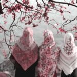 Three Muslim women wearing hijab stand together beneath flowering branches, reflecting on Islam and modernity beyond Western liberal values.