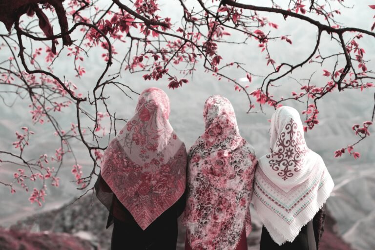 Three Muslim women wearing hijab stand together beneath flowering branches, reflecting on Islam and modernity beyond Western liberal values.